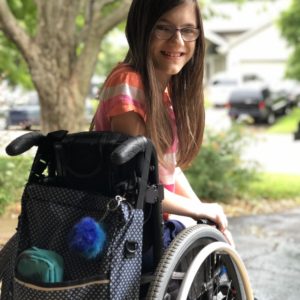 Girl sitting on her wheelchair looking back and smiling at camera